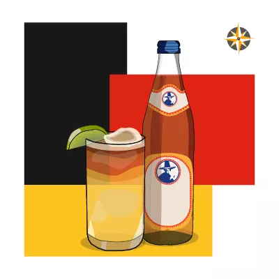 Cocktail berlinese Tschunk con bottiglia di Club Mate e bicchiere con lime, su sfondo brutalista nei colori della bandiera tedesca